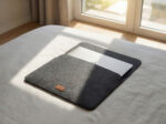 Soft grey laptop cover lying on a white bed sheet.